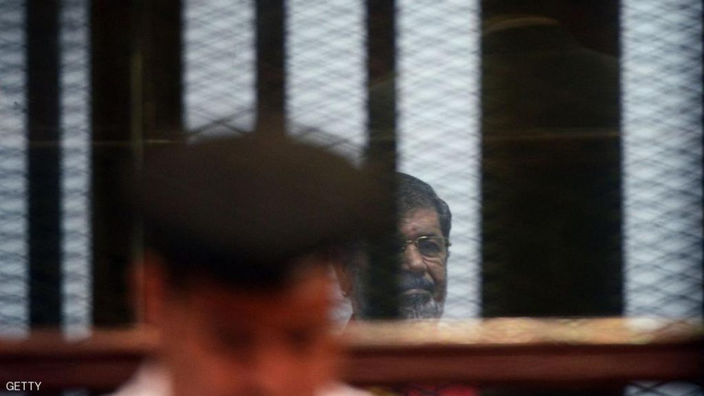 Egypt's ousted Islamist president Mohamed Morsi, wearing a red uniform, looks on from behind the defendant's bars during his trial on espionage charges at a court in Cairo on June 18, 2016. An Egyptian court sentenced Morsi to life in prison in an espionage trial in which six co-defendants were handed death penalties.The court acquitted Morsi of charges of having supplied Qatar with classified documents but sentenced him to life for leading an unlawful organisation.  / AFP / MOHAMED EL-SHAHED        (Photo credit should read MOHAMED EL-SHAHED/AFP/Getty Images)